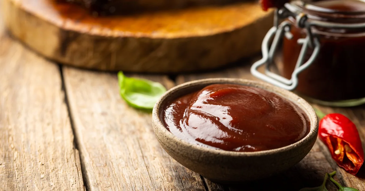 Three small jars of barbecue sauce on a wooden board
