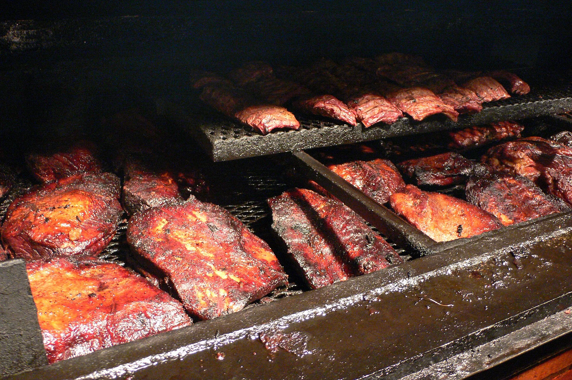 A whole smoked brisket with a black peppery bark resting on pink butcher paper, one slice lifted to show the moist interior