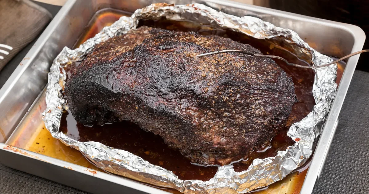 A whole barked brisket resting in a foil-lined tray