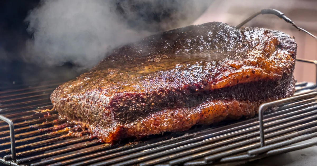 A brisket smoking on a grate with wisps of smoke rising
