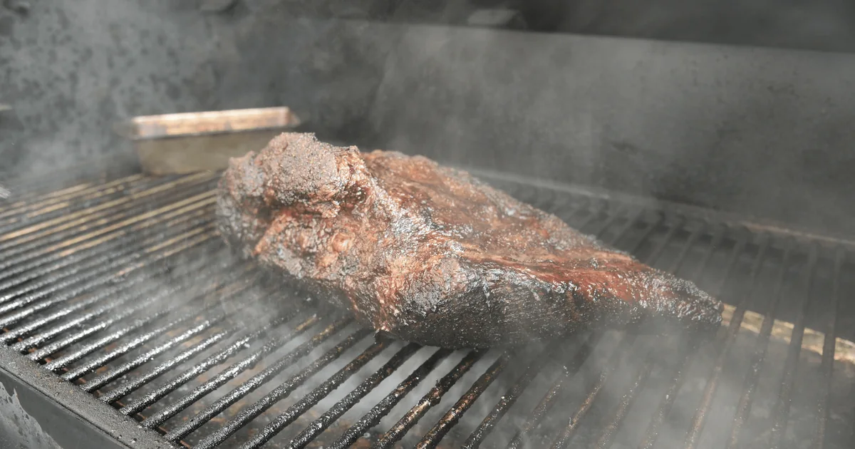 A brisket cooking on a smoker grate with smoke rising