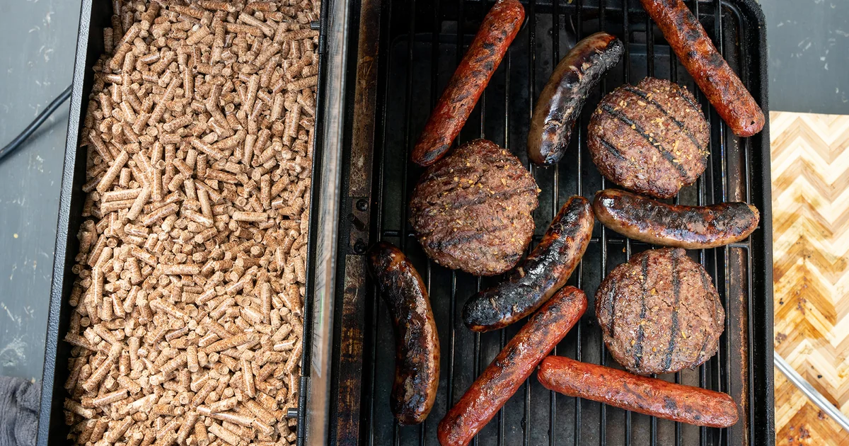 A grill grate with sausages beside a bed of wood pellets