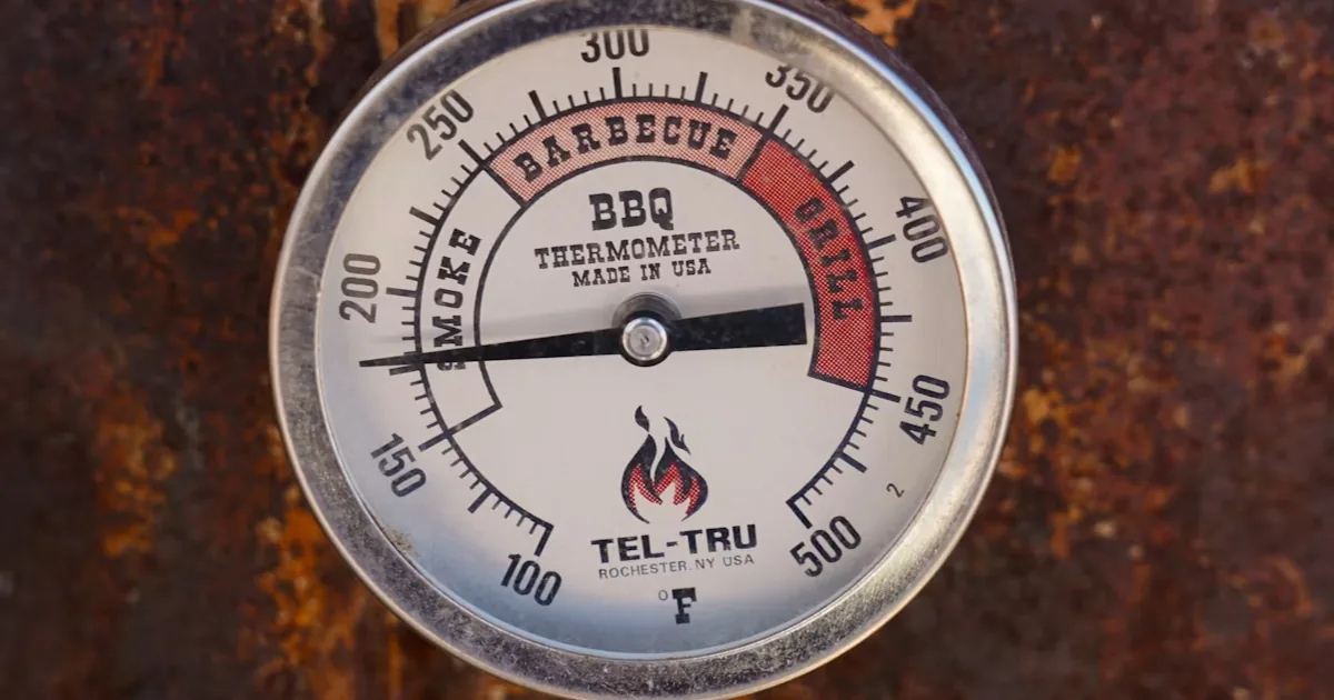 A close-up of a smoker dial and grate-level thermometer probe showing a low-and-slow temperature setting