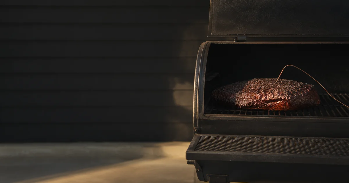 A smoked brisket cooking in an open black offset smoker with a temperature probe